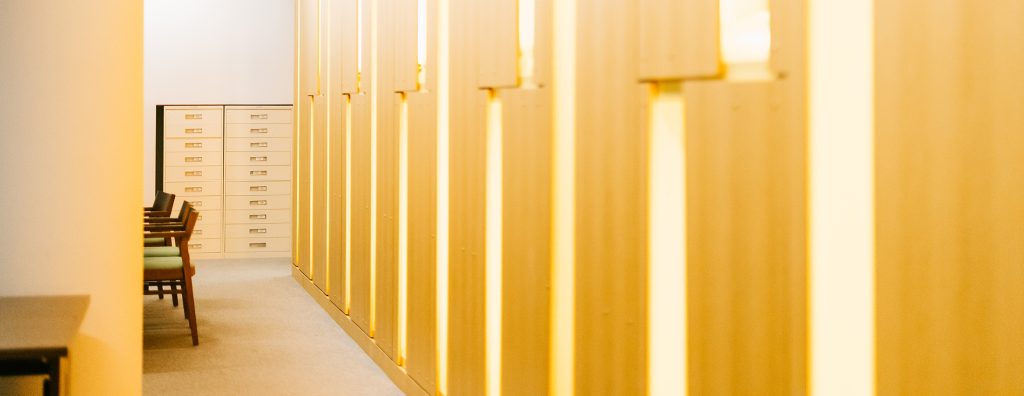 abstract photo of library wall, with chairs on the lefthand side and light peaking through wooden panels