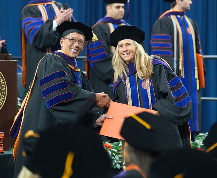 Dean Terrence Lau shakes the hand of a graduate and hands her an orange diploma