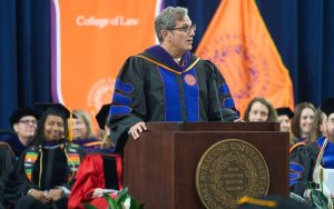 Frank Ryan speaks to the graduates from a podium at Law Commencement 2025, wearing regalia with his hands on the podium