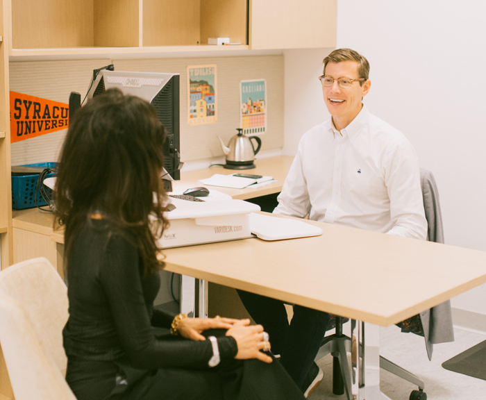 Two people sit across a desk from each other and have a discussion in an office