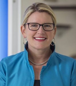 headshot of joanna smiling at the camera with black glasses and blue jacket