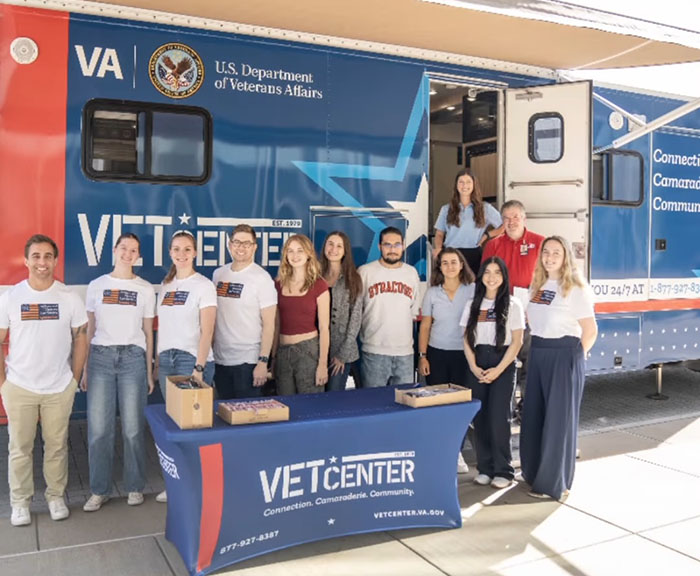 Syracuse Law and Falk students stand in front of a Vet Center table with a blue tablecloth and giveaways on it at an event